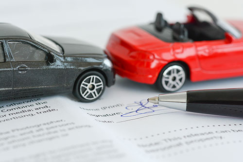 two toys cars in pretend accident on paperwork with a pen | Colorado Car Insurance Law