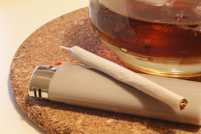 a joint laying on a lighter next to a glass of booze