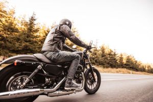 man in leather jacket riding a Harley in the woods
