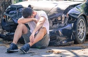 man sitting and crying in front of damaged car after crash | Car Accident PTSD