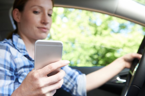 woman holding looking at cell phone while driving | Distracted Driving Accidents