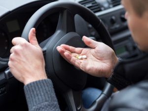 man behind drivers wheel with pills in hand | How Dangerous is Driving High